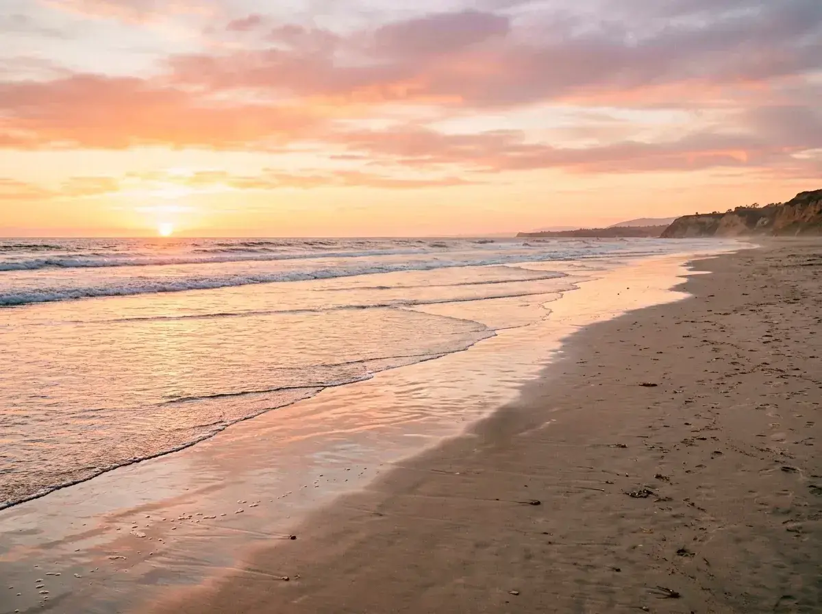 An empty beach at sunset with waves washing onto the shore and no people visible on the sand.
