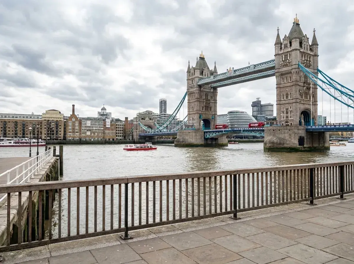 A paved walkway and wooden railing are empty of people, showing an unobstructed view of the River Thames and Tower Bridge.