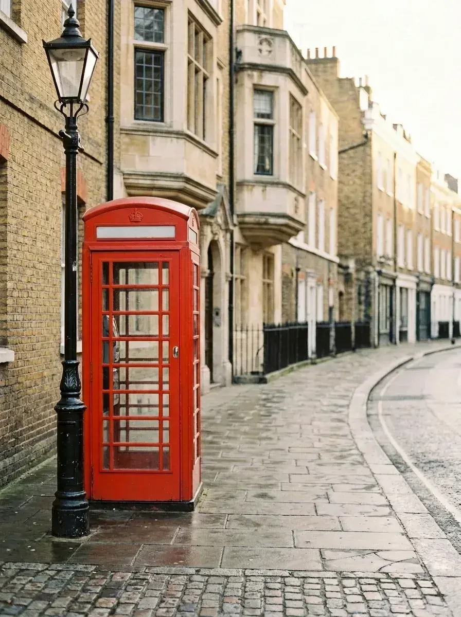 A red telephone booth and a black lamppost stand on an empty sidewalk in front of brick buildings.