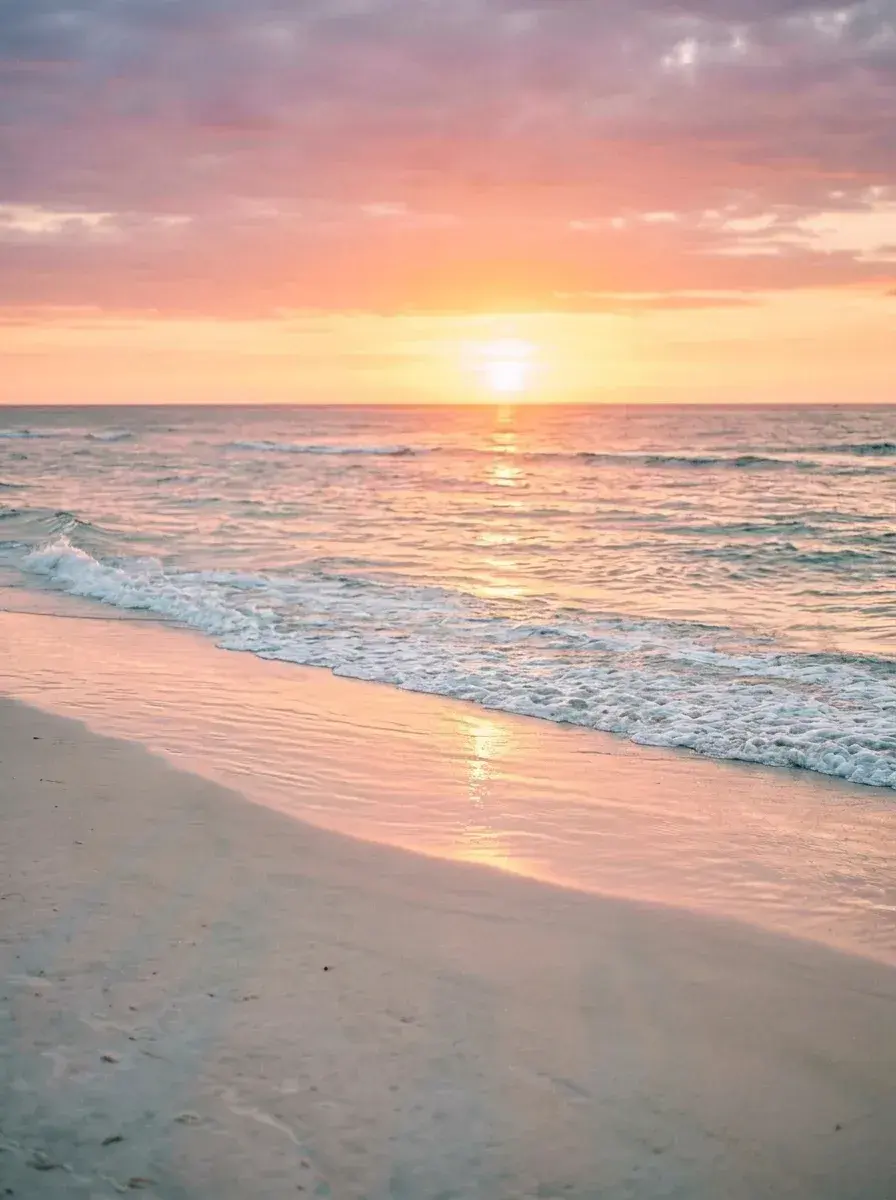 A sunset view of a beach with waves washing onto the sand and no people in sight.