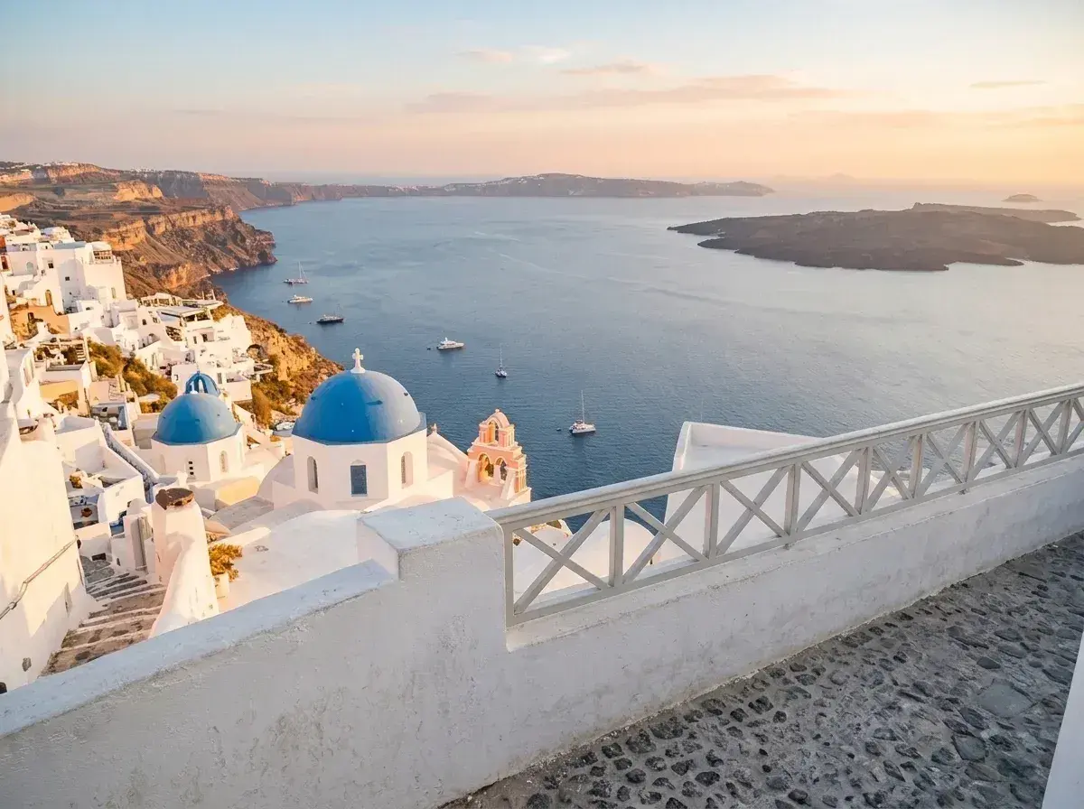 An empty stone walkway overlooks the white buildings and blue-domed churches of Santorini.